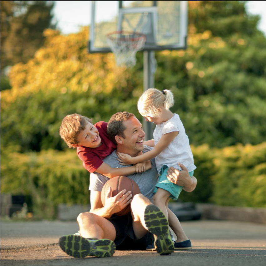father hugging two children on basketball court, laughing